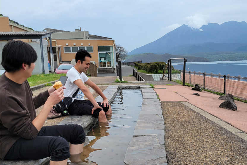 桜島をバッグに足湯に入っている